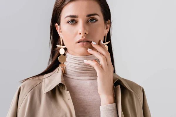 Beautiflul, stylish girl touching face while looking at camera isolated on grey — Stock Photo