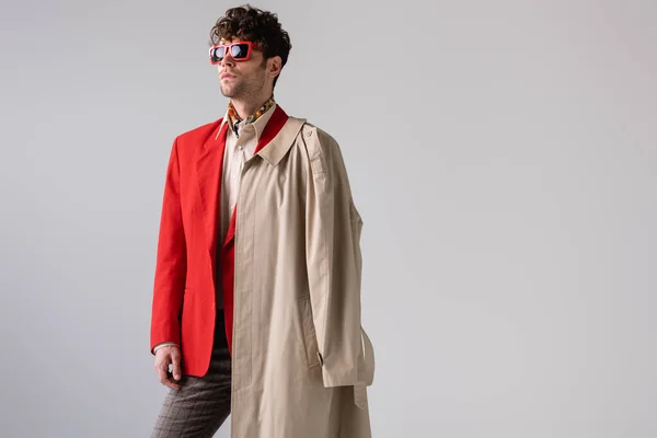 Homem da moda com casaco de trincheira no ombro olhando para longe isolado em cinza — Fotografia de Stock