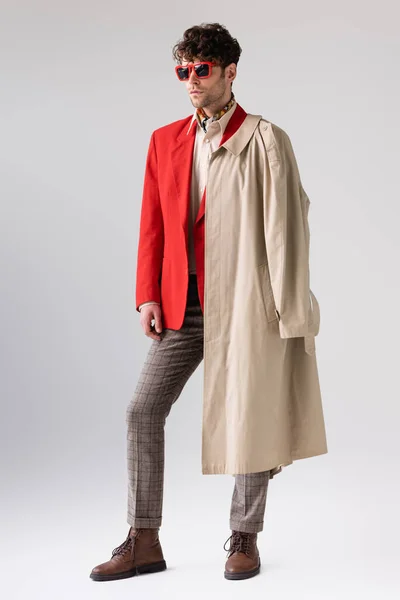 Visão de comprimento total da moda, homem confiante com casaco de trincheira sobre ombro olhando para longe no cinza — Fotografia de Stock