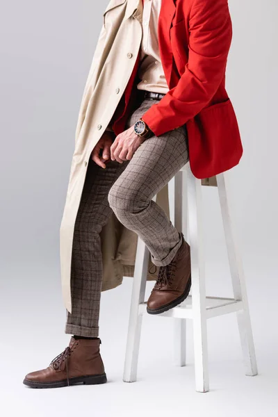 Cropped view of stylish man in autumn outfit sitting on stool on grey — Stock Photo