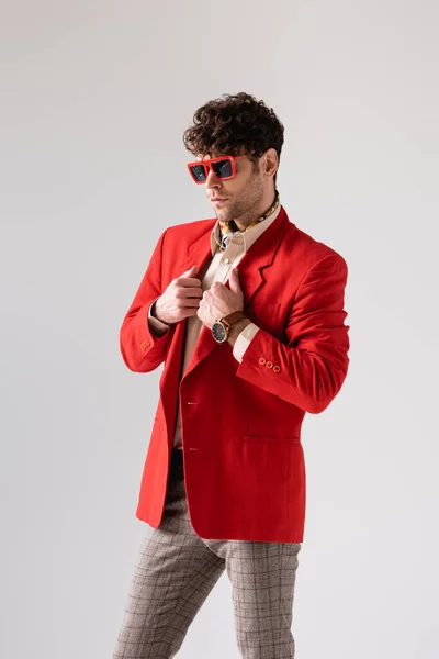 Hombre de moda en gafas de sol tocando chaqueta roja aislada en gris - foto de stock