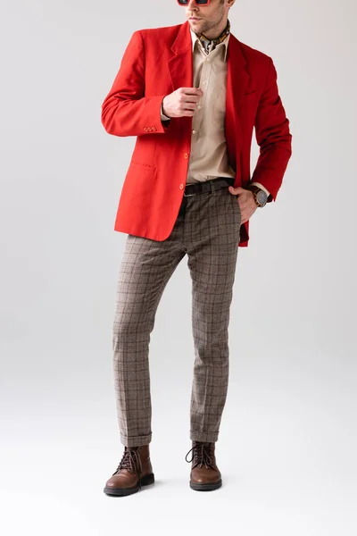 Cropped view of stylish man holding hand in pocket and touching red blazer on grey — Stock Photo