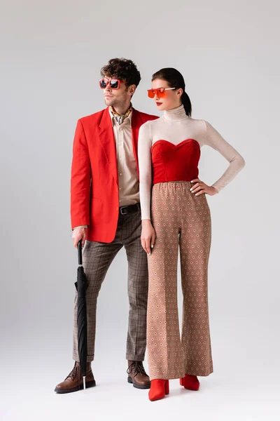 Full length view of stylish couple in sunglasses looking away on grey — Stock Photo