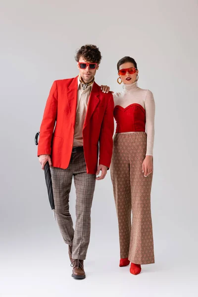 Full length view of stylish girl and trendy man with folded umbrella walking on grey — Stock Photo