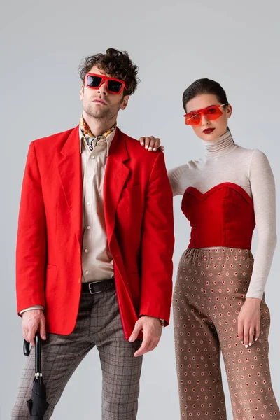 Elegante donna che tocca la spalla dell'uomo di tendenza mentre posa isolata sul grigio — Stock Photo