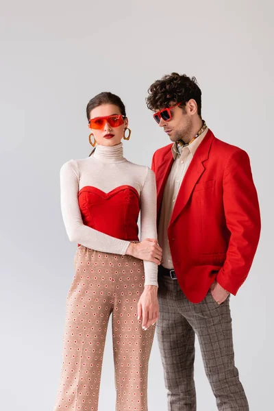 Pareja joven de moda en gafas de sol posando aislados en gris - foto de stock