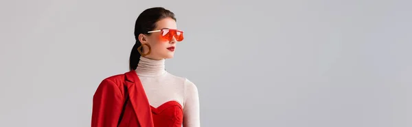 Plan panoramique de fille élégante en lunettes de soleil rouges regardant loin isolé sur gris — Photo de stock