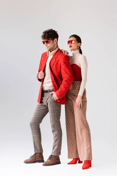 Full length view of elegant girl touching shoulder of trendy man in red blazer on grey — Stock Photo