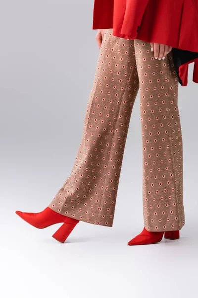 Vue recadrée de fille tendance en pantalon beige et bottes rouges sur gris — Photo de stock