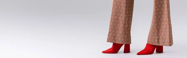 Обрезанный вид стильной женщины в бежевых брюках и красных сапогах на сером, горизонтальном изображении — стоковое фото