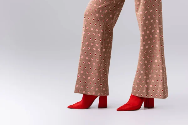 Частичный вид стильной женщины в бежевых брюках и красных сапогах на сером — стоковое фото