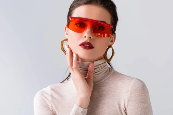Привлекательная девушка в солнечных очках, касающаяся лица, глядя на камеру, изолированную на сером — стоковое фото