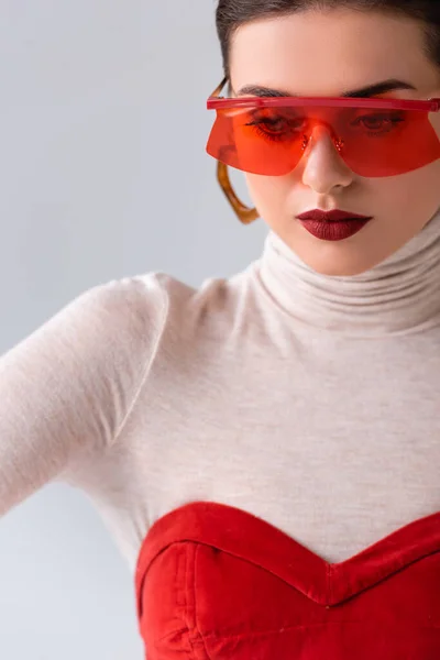 Красивая, стильная девушка в красных солнцезащитных очках, позирующая изолированной на сером — стоковое фото