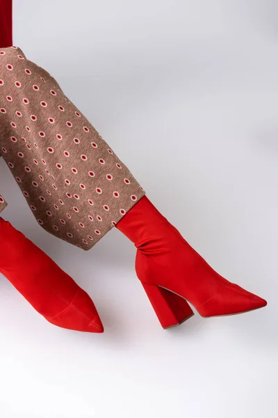 Cropped view of trendy woman in beige trousers and red boots sitting on white floor — Stock Photo