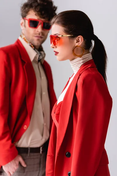 Selective focus of stylish woman and trendy man in red blazers and sunglasses isolated on grey — Stock Photo