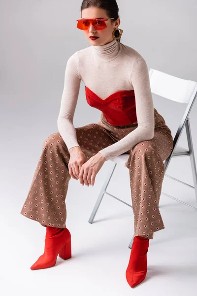 Mulher na moda inclinada para a frente e olhando para longe, sentada na cadeira em cinza — Fotografia de Stock