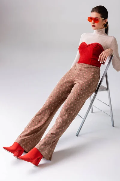 Mujer elegante mirando hacia otro lado, sentado en la silla con las piernas extendidas en gris - foto de stock