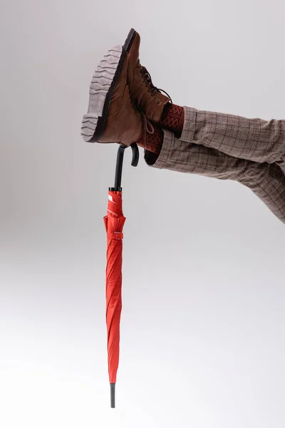 Обрезанный вид человека с вытянутыми ногами, опирающегося на красный зонтик на сером — стоковое фото