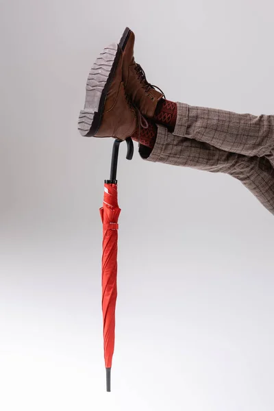 Cropped view of man with extended legs leaning on red umbrella on grey — Stock Photo