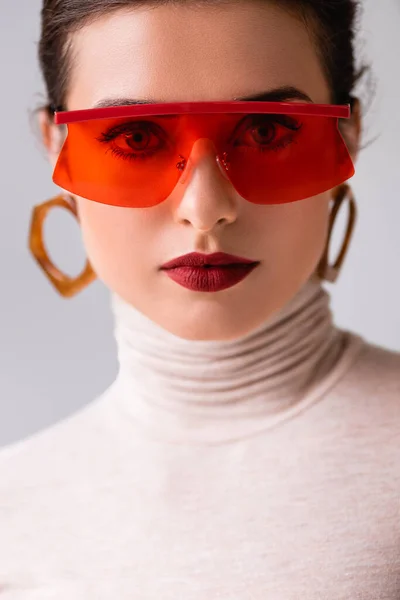 Portrait de belle femme aux lunettes de soleil rouges regardant la caméra isolée sur gris — Photo de stock