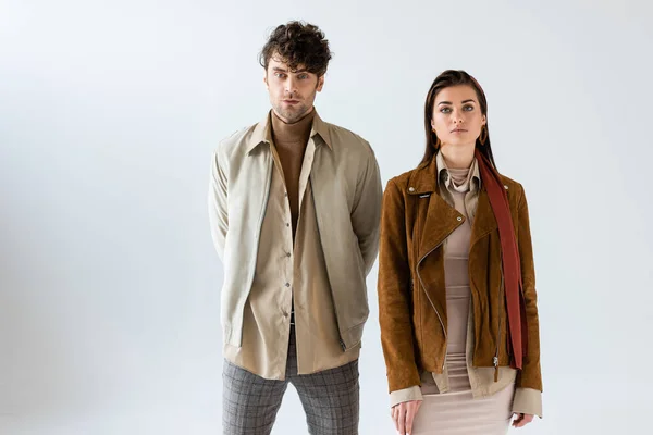 Femme et homme élégants en tenue d'automne regardant la caméra et debout ensemble sur le gris — Photo de stock