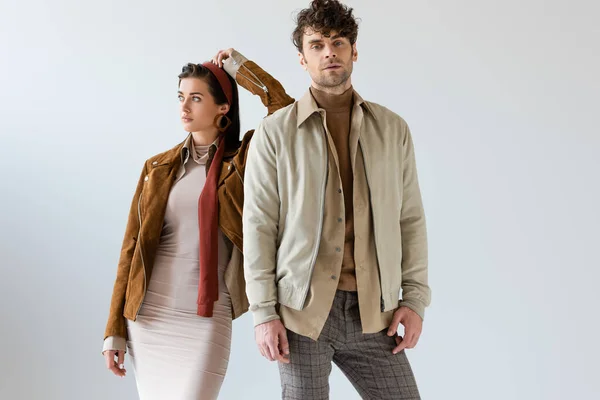 Attractive woman looking away and leaning on handsome man in autumn outfit on grey — Stock Photo