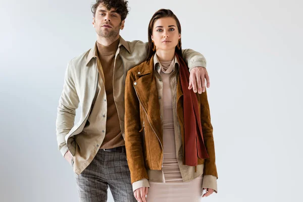 Stylish man with hand in pocket embracing attractive woman standing near on grey — Stock Photo