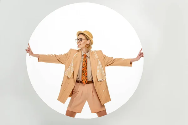 Smiling woman in beige blazer and straw hat touching round hole on white background — Stock Photo