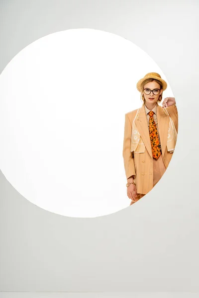 Hermosa chica en sombrero de paja y chaqueta beige mirando a la cámara al lado del círculo sobre fondo blanco - foto de stock