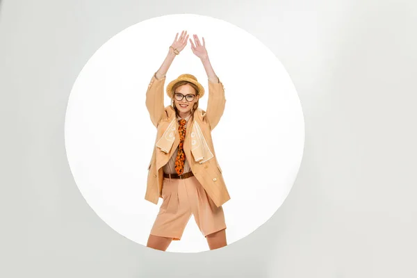 Cheerful stylish girl in straw hat with raised hands standing near circle on white background — Stock Photo