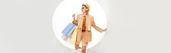 Image horizontale d'une femme souriante tenant des sacs à provisions près d'un trou rond sur fond blanc — Photo de stock