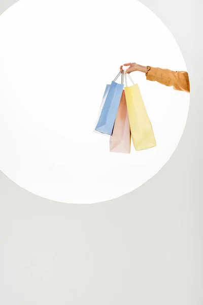 Copped view of woman holding colorful shopping bags behind round hole on white background — Stock Photo