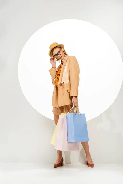 Hermosa modelo mirando a la cámara y sosteniendo bolsas de compras cerca del círculo sobre fondo blanco - foto de stock