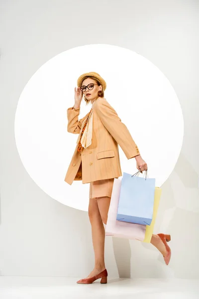 Atractiva chica elegante sosteniendo bolsas de compras y caminando cerca del círculo sobre fondo blanco - foto de stock