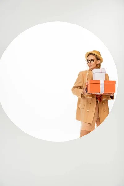 Smiling woman holding gift boxes behind round hole on white background — Stock Photo