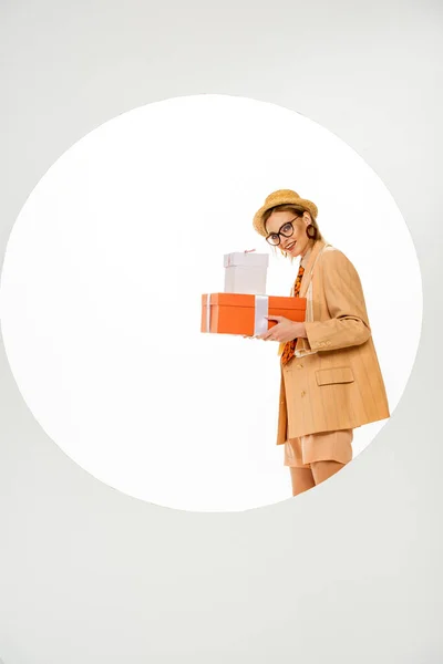 Menina elegante sorrindo para a câmera e segurando caixas de presente atrás círculo no fundo branco — Fotografia de Stock