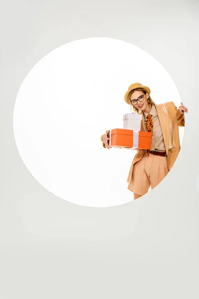 Модна жінка посміхається, тримаючи подарунки біля круглої діри на білому тлі — стокове фото