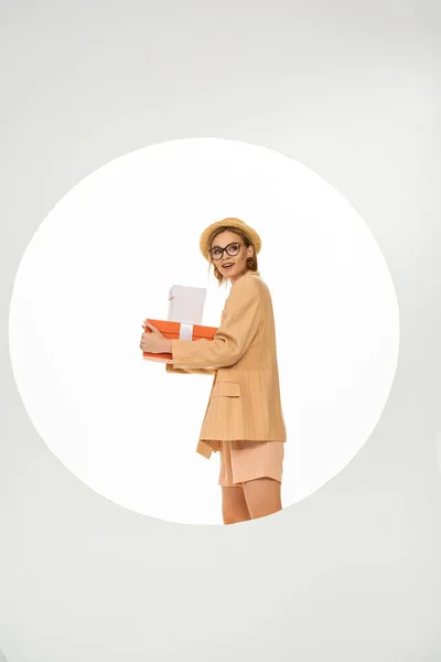 Side view of smiling girl in beige jacket and straw hat holding presents on white background — Stock Photo