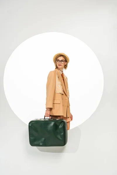 Menina elegante bonita segurando saco de viagem verde perto do círculo no fundo branco — Fotografia de Stock