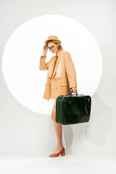 Mujer positiva de moda sosteniendo bolsa de viaje verde cerca del círculo sobre fondo blanco - foto de stock