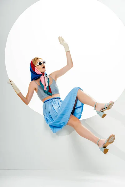 Femme à la mode en lunettes de soleil et foulard posant dans un trou rond sur fond blanc — Photo de stock