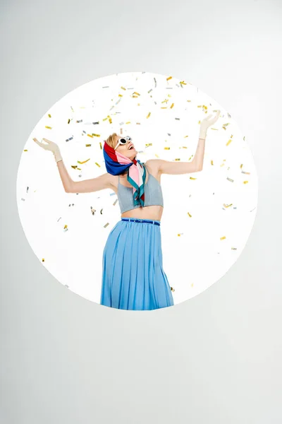 Cheerful woman in sunglasses and headscarf standing under falling confetti in circle on white background — Stock Photo