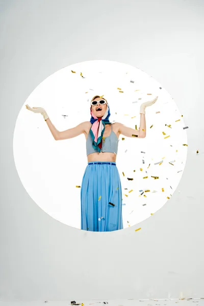 Потрясенная стильная женщина, стоящая под падающими конфетти возле круга на белом фоне — стоковое фото