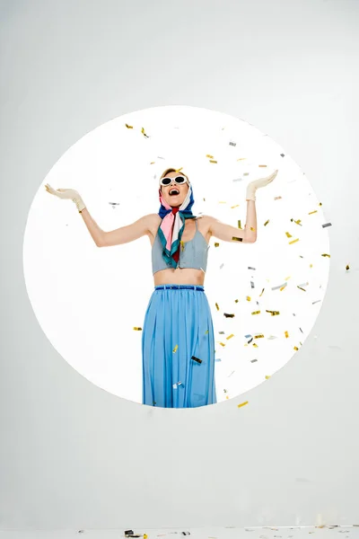 Shocked stylish woman standing under falling confetti near circle on white background — Stock Photo