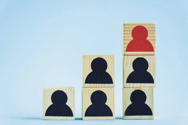 Pyramid of wooden blocks with black and red human icons on blue background, leadership concept — Stock Photo