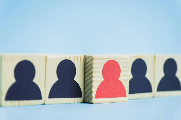 Fila de bloques de madera con iconos humanos negros y rojos sobre fondo azul, concepto de liderazgo - foto de stock