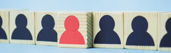 Rangée de blocs de bois avec des icônes humaines noires et rouges sur fond bleu, concept de leadership, plan panoramique — Photo de stock