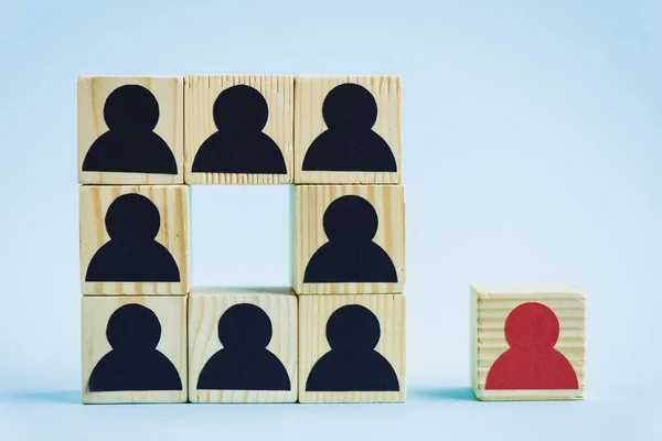 Cuadrado de bloques de madera con iconos humanos negros y pieza roja sobre fondo azul, concepto de liderazgo - foto de stock