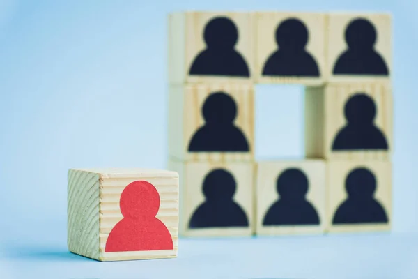 Cuadrado de bloques de madera con iconos humanos negros y pieza roja sobre fondo azul, enfoque selectivo - foto de stock