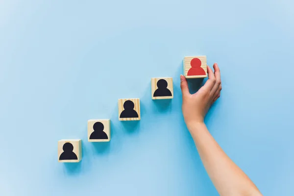 Visão parcial de mão e blocos de madeira com ícones humanos preto e vermelho no fundo azul, conceito de liderança — Fotografia de Stock